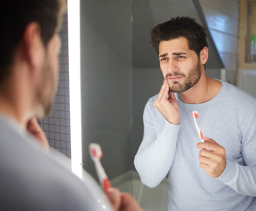 man holding toothbrush and jaw in pain