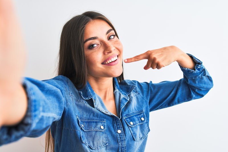 a young woman wearing a denim shirt pointing to her smile that has recently been whitened