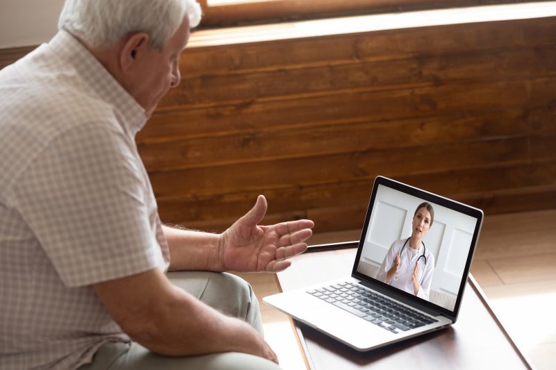 an older man sitting in front of a computer talking to his dentist