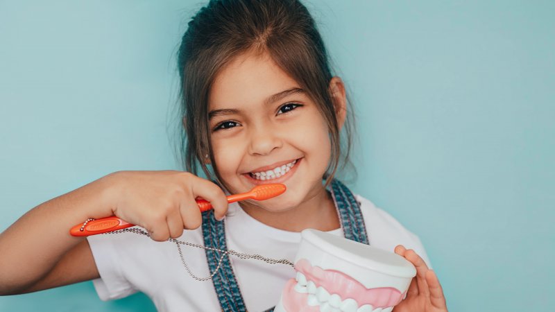 a little girl brushing her teeth using a toothbrush and holding a mouth mold